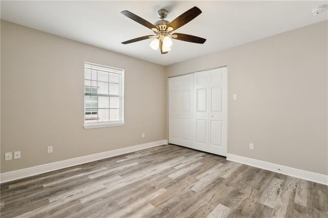 unfurnished bedroom featuring ceiling fan, a closet, baseboards, and wood finished floors