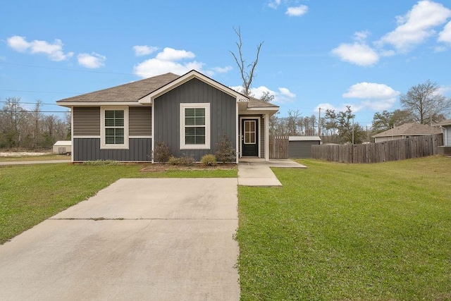 view of front of property with board and batten siding, a shingled roof, a front yard, and fence