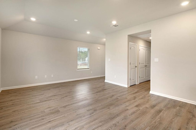 empty room with visible vents, baseboards, vaulted ceiling, recessed lighting, and wood finished floors