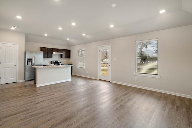 kitchen featuring an island with sink, under cabinet range hood, appliances with stainless steel finishes, light countertops, and lofted ceiling