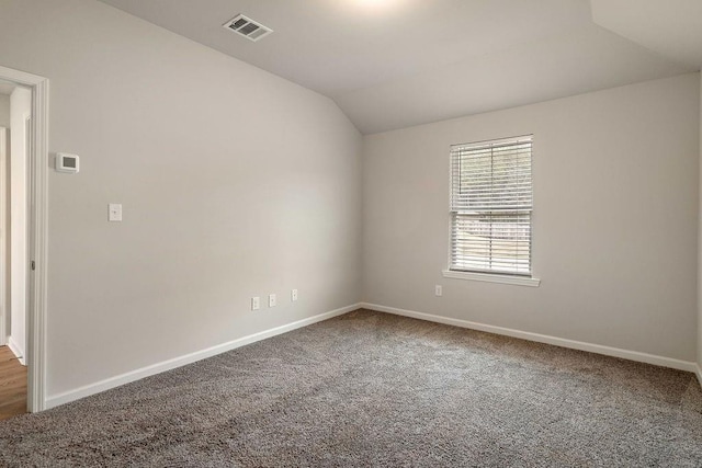 carpeted spare room featuring vaulted ceiling, baseboards, and visible vents