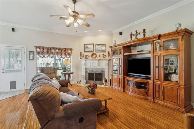 living area featuring visible vents, light wood-style flooring, a ceiling fan, ornamental molding, and a fireplace