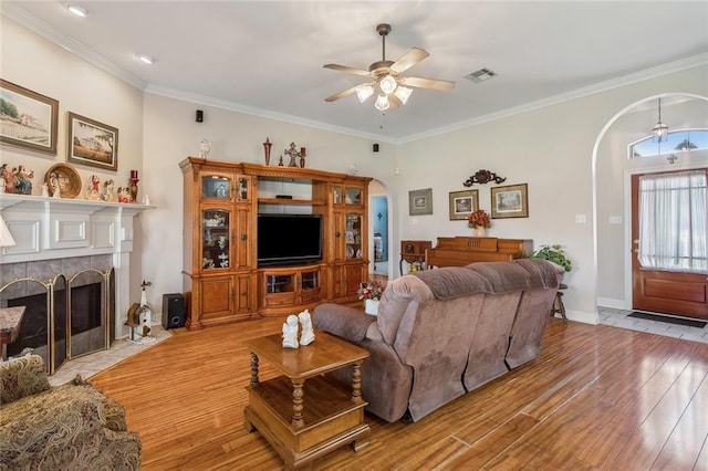 living area with a tiled fireplace, crown molding, light wood-style flooring, and arched walkways