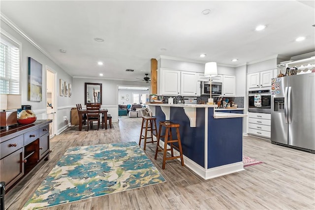 kitchen with a breakfast bar, white cabinetry, stainless steel appliances, a peninsula, and crown molding