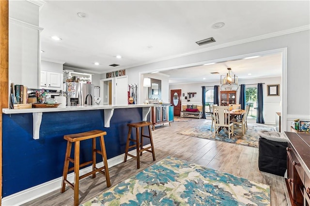 kitchen with crown molding, stainless steel fridge with ice dispenser, visible vents, and light wood finished floors