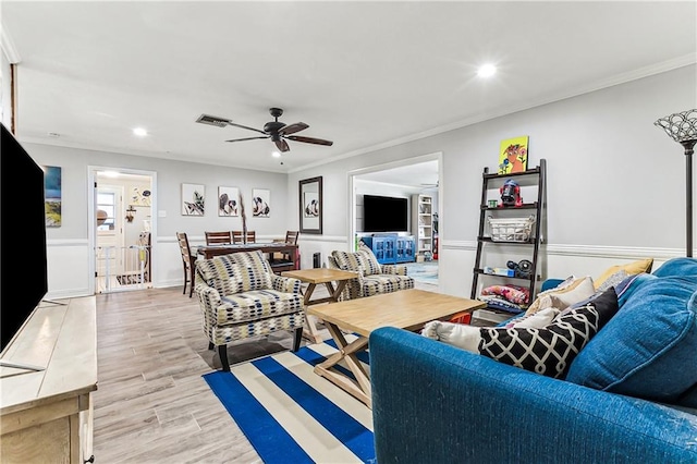 living area with light wood-type flooring, visible vents, a wainscoted wall, and crown molding