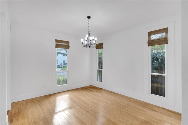 spare room featuring baseboards, a notable chandelier, and light wood finished floors