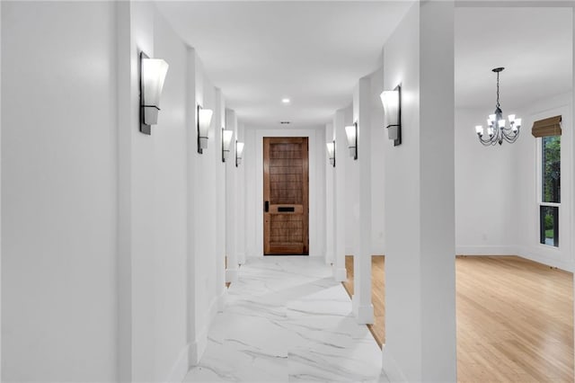 hall featuring baseboards, marble finish floor, and an inviting chandelier