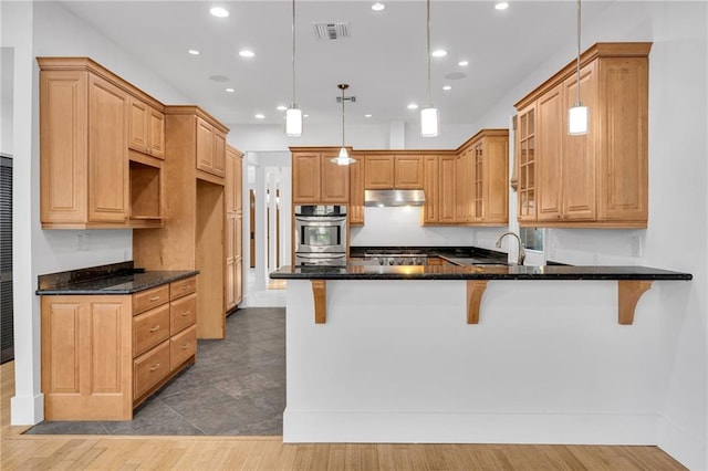 kitchen featuring visible vents, under cabinet range hood, dark stone countertops, a peninsula, and glass insert cabinets