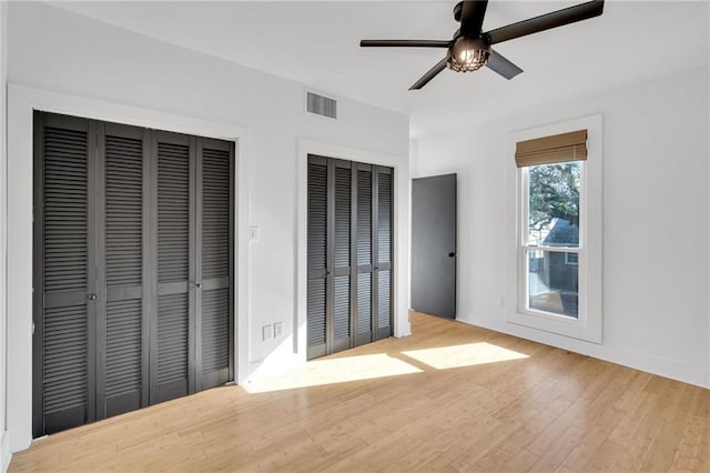 unfurnished bedroom featuring wood finished floors, baseboards, visible vents, ceiling fan, and multiple closets