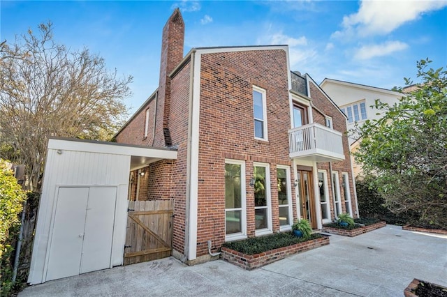 exterior space featuring a balcony, a gate, brick siding, and a chimney