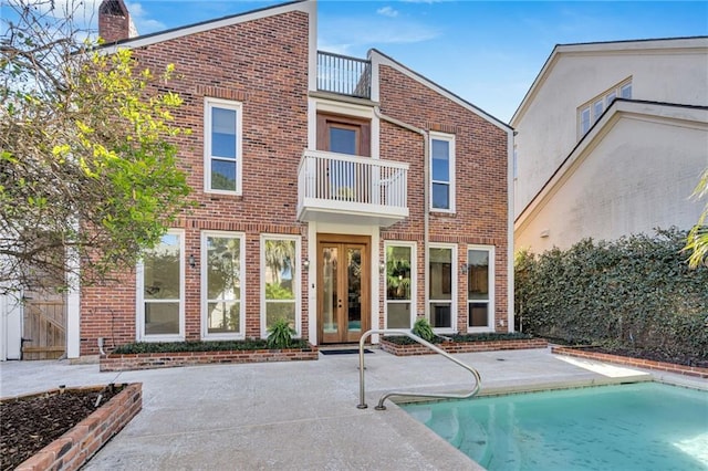 rear view of property featuring an outdoor pool, a balcony, french doors, and brick siding