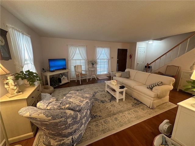 living area featuring dark wood-style floors, a textured ceiling, and stairs