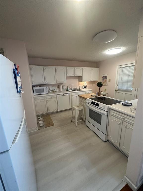 kitchen with light wood-style flooring, a sink, white appliances, white cabinets, and light countertops