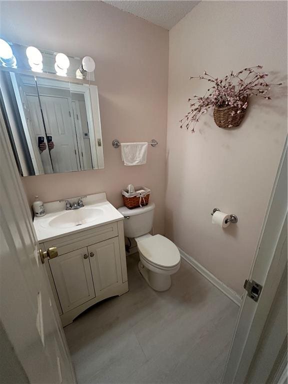 bathroom featuring vanity, toilet, baseboards, and a textured ceiling