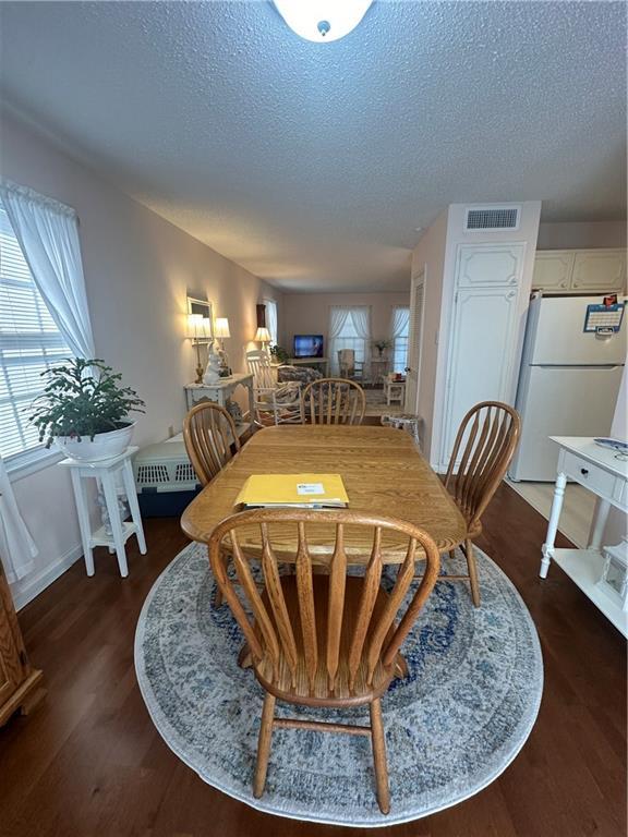 dining room with wood finished floors, visible vents, a wealth of natural light, and a textured ceiling