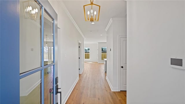 hallway featuring a notable chandelier, baseboards, light wood-style floors, and crown molding