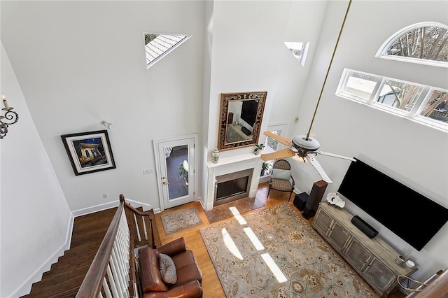 living area featuring baseboards, wood finished floors, a towering ceiling, and a fireplace