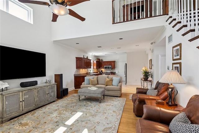 living room with crown molding, baseboards, light wood-type flooring, a towering ceiling, and a ceiling fan