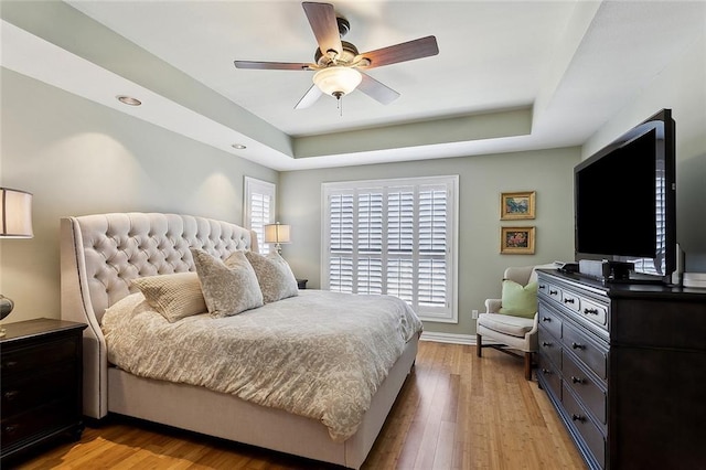 bedroom with light wood-style flooring, baseboards, a tray ceiling, and ceiling fan