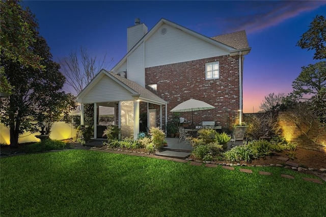 rear view of property with brick siding, a lawn, a chimney, a sunroom, and a patio