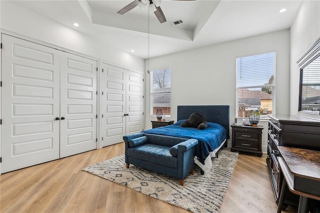 bedroom featuring light wood-type flooring, a raised ceiling, two closets, and multiple windows