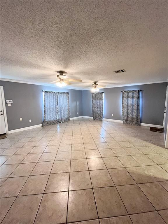 empty room with light tile patterned floors, baseboards, a textured ceiling, and a ceiling fan