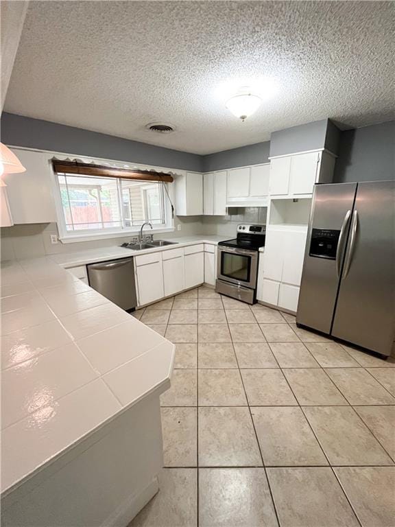 kitchen featuring visible vents, a sink, tile countertops, stainless steel appliances, and white cabinets