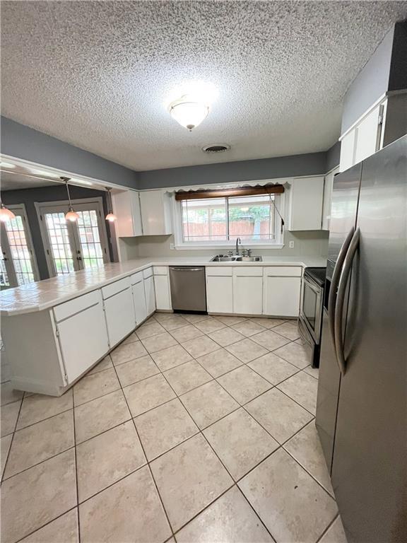 kitchen featuring appliances with stainless steel finishes, a peninsula, light tile patterned flooring, white cabinets, and a sink