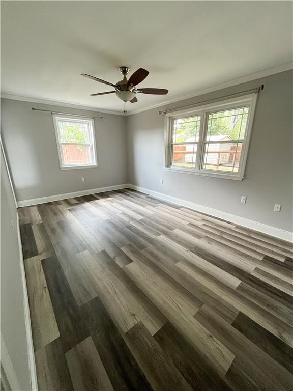 empty room with wood finished floors, baseboards, and ornamental molding