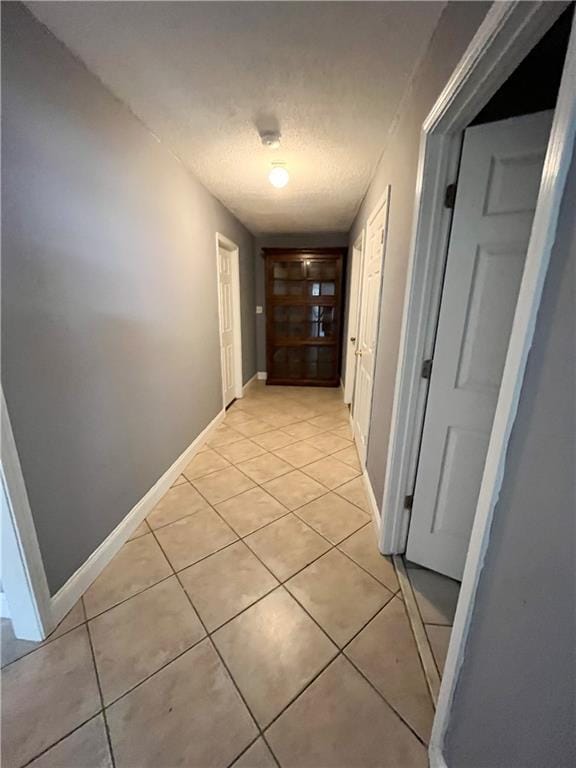 corridor featuring light tile patterned floors, baseboards, and a textured ceiling