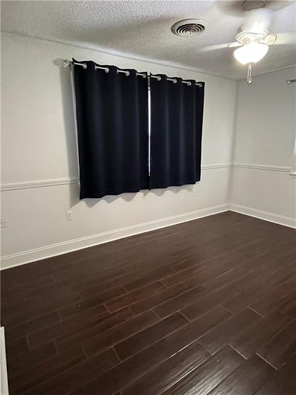 spare room with dark wood-style floors, visible vents, a textured ceiling, and baseboards