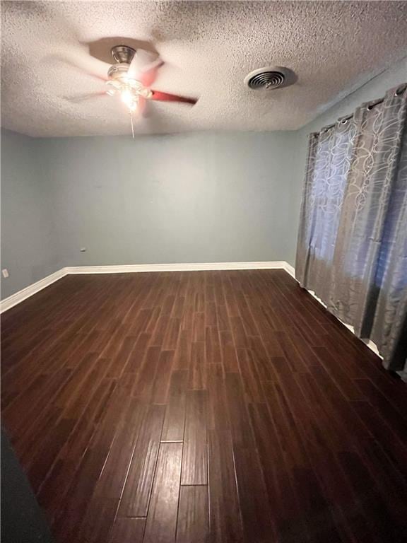 unfurnished room featuring baseboards, visible vents, dark wood-style flooring, and ceiling fan