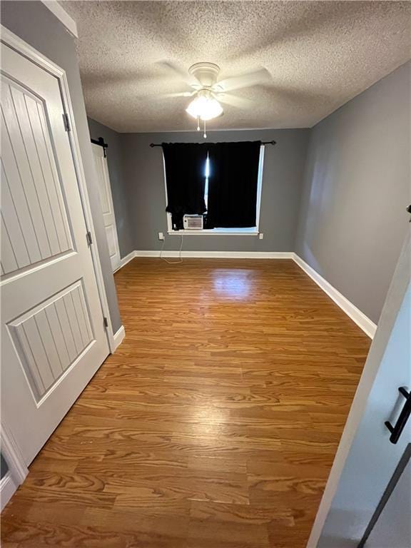 unfurnished bedroom with a barn door, wood finished floors, baseboards, and ceiling fan