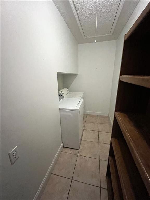 laundry area with washer and clothes dryer, a textured ceiling, light tile patterned floors, baseboards, and attic access