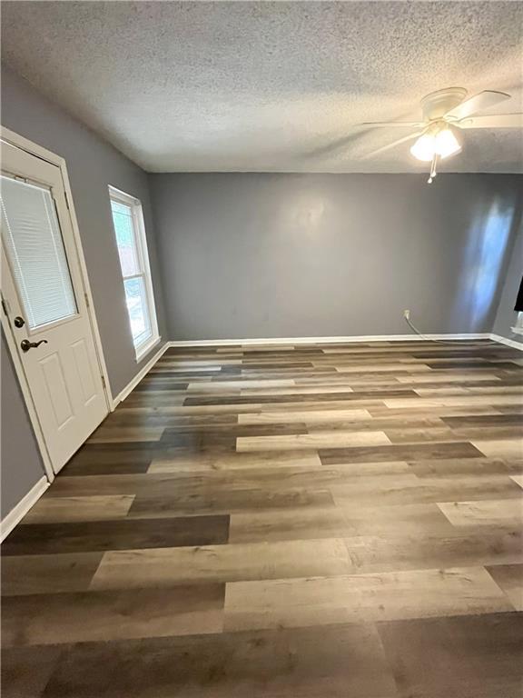 unfurnished room featuring a ceiling fan, wood finished floors, baseboards, and a textured ceiling