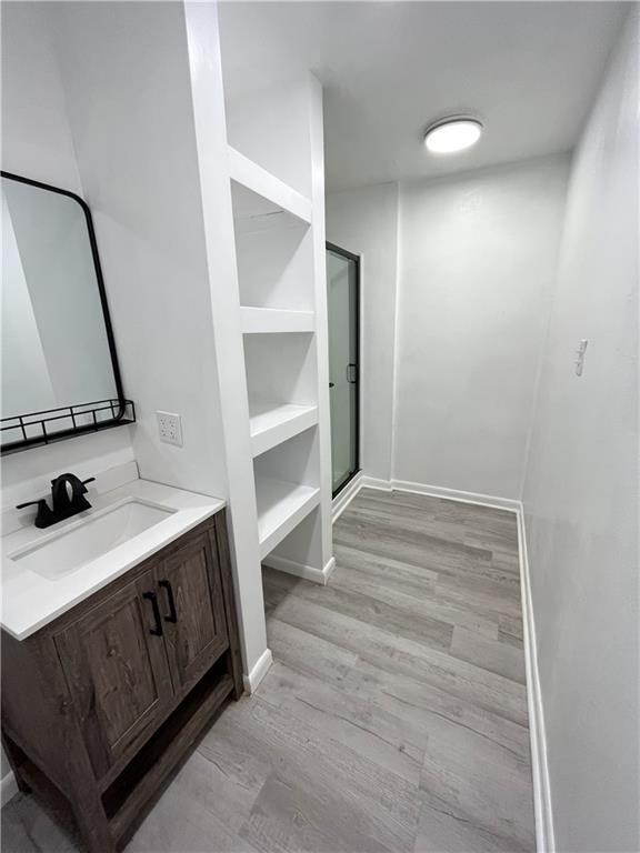 bathroom with baseboards, wood finished floors, a stall shower, and vanity