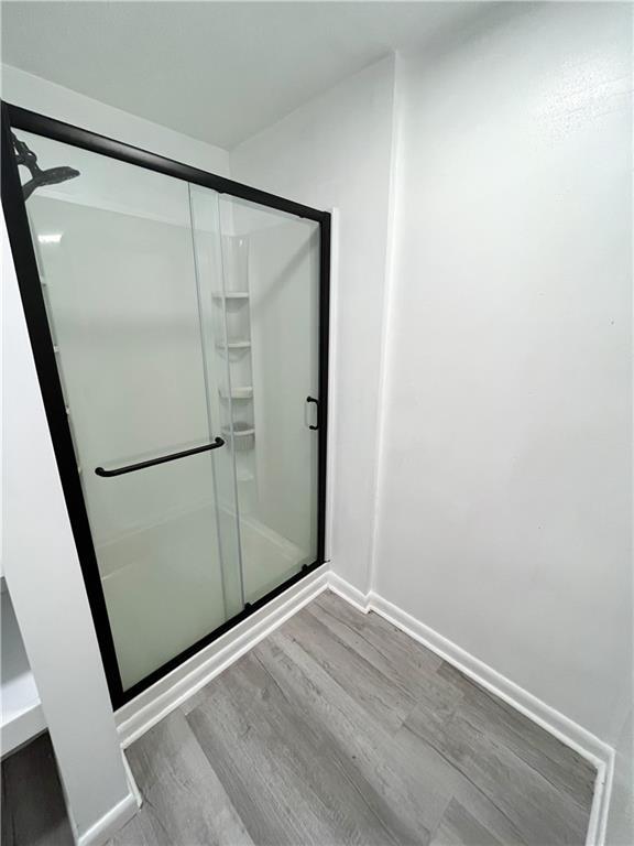 full bath featuring baseboards, wood finished floors, and a shower stall