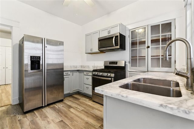 kitchen with gray cabinetry, light stone countertops, light wood-type flooring, stainless steel appliances, and a sink