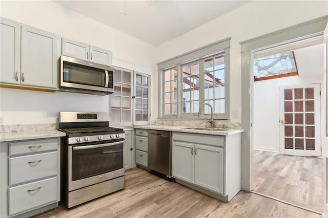 kitchen with a wealth of natural light, gray cabinetry, a sink, light wood-style floors, and appliances with stainless steel finishes