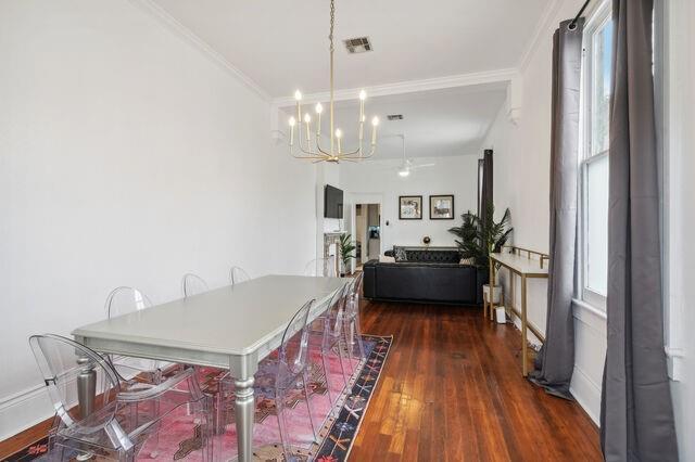 dining area with dark wood finished floors, crown molding, a notable chandelier, and visible vents