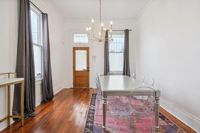 dining area featuring a notable chandelier, baseboards, dark wood-type flooring, and ornamental molding