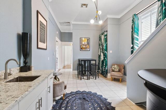 interior space featuring visible vents, a sink, white cabinets, crown molding, and light tile patterned floors