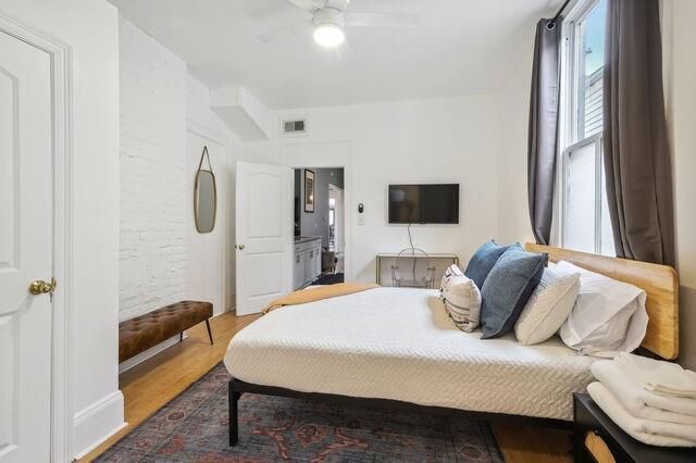 bedroom with ceiling fan, visible vents, and wood finished floors