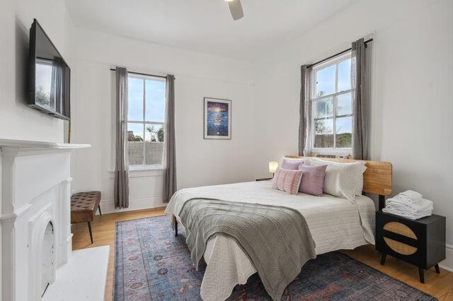 bedroom with a fireplace, wood finished floors, and ceiling fan