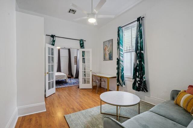 living area featuring wood finished floors, visible vents, baseboards, ceiling fan, and french doors