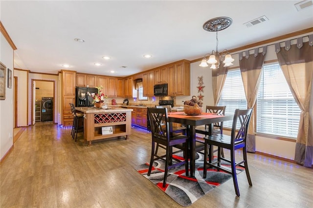 dining area with visible vents, light wood-style flooring, ornamental molding, a notable chandelier, and independent washer and dryer