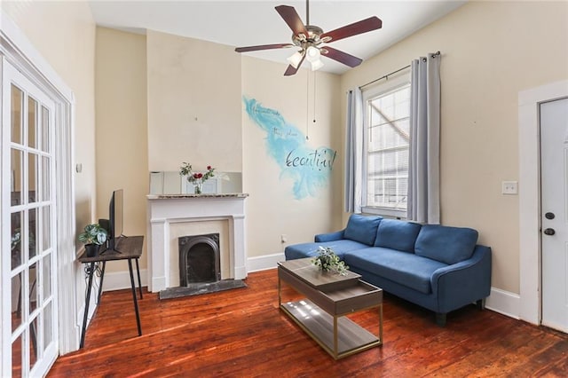 living area featuring a ceiling fan, wood finished floors, baseboards, and a fireplace with raised hearth