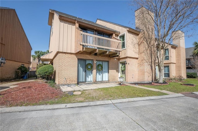 view of front of home featuring a front yard, a balcony, brick siding, and a chimney