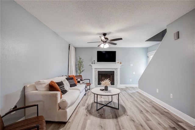 living area with light wood finished floors, baseboards, ceiling fan, and a premium fireplace